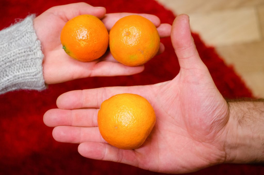 2 offene Hände von unterschiedlichen Personen nebeneinander: Eine mit einer Orange die andere mit 2 Orangen